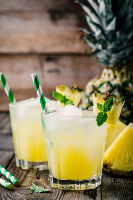 Fresh pineapple juice in two glasses with ice and mint leaves on dark rustic background