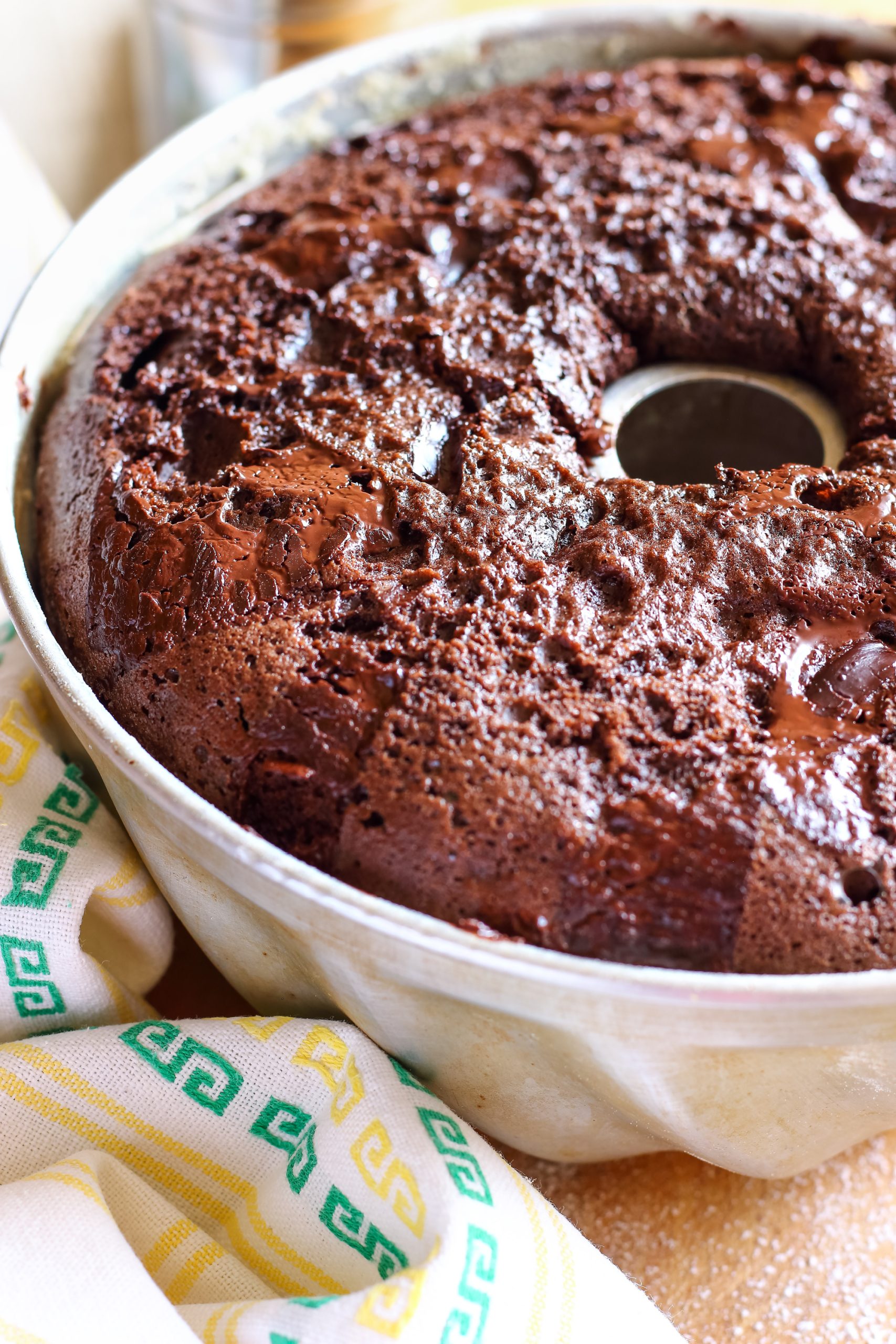 An Irish Cream chocolate bundt cake in a metal pan, partially veiled by a patterned cloth.