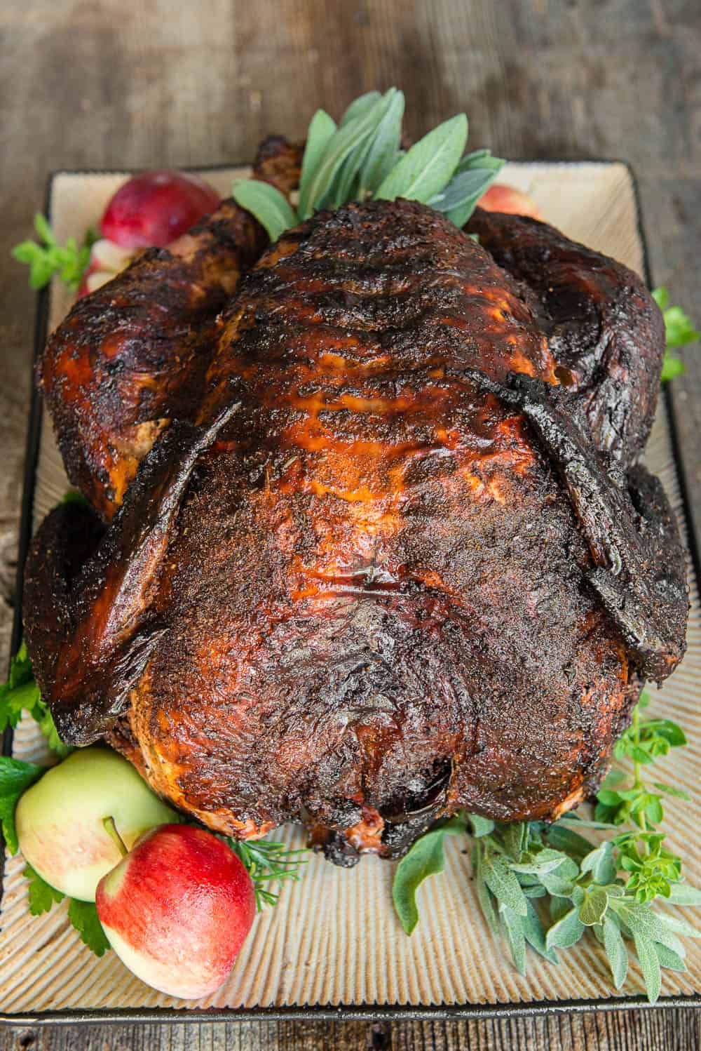 Smoked whole turkey on a platter with fresh herbs and apples, showcased on a wooden table—truly one of the best turkey recipes for any festive gathering.