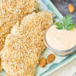 almond crusted chicken tenders on a plate with dipping sauce.