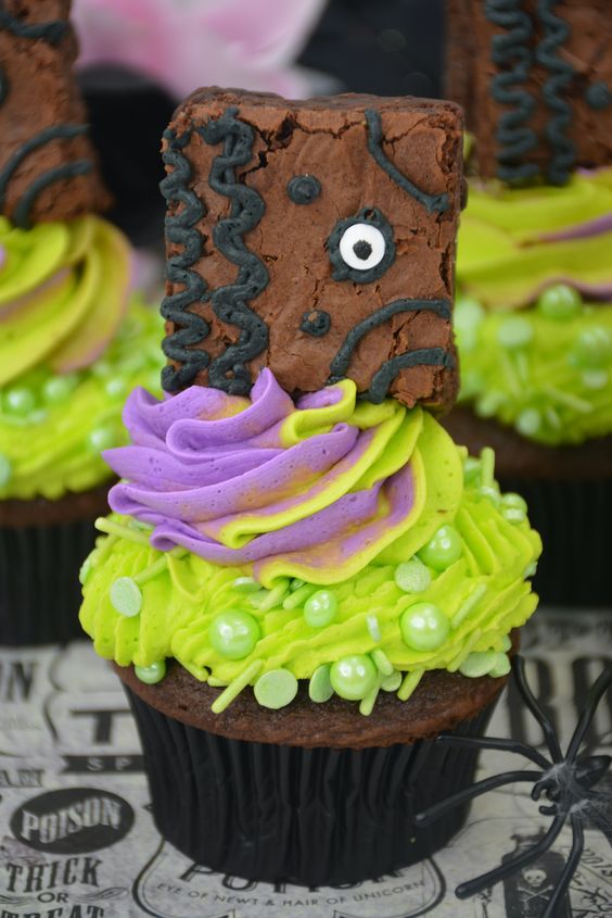 A cupcake decorated with bright green and purple frosting, topped with a brownie piece designed to resemble Frankenstein's face—perfectly creepy Halloween food that's delightfully creative.