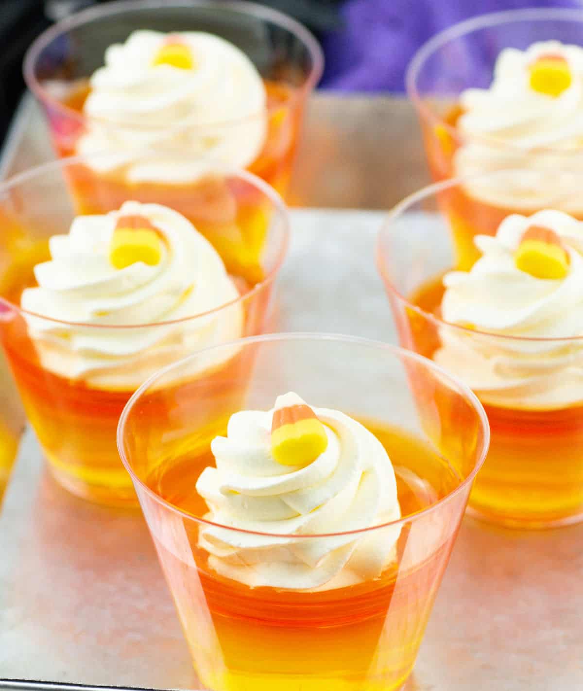 Clear cups filled with layered orange, yellow, and white dessert, topped with whipped cream and a piece of candy corn make for some creative Halloween treats.