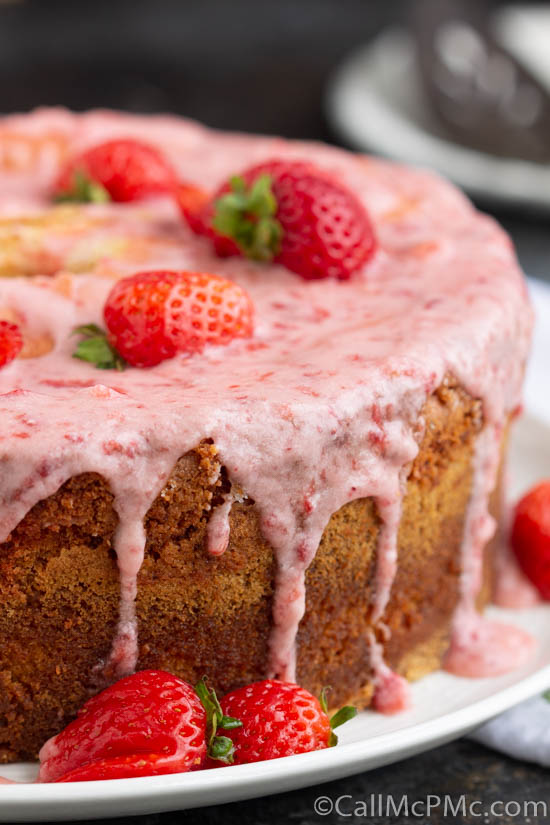 A strawberry cake with icing, strawberries, and cream on a plate.