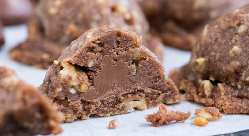 A close-up of a Chocolate Secret Kiss Cookie reveals a dessert with a crunchy exterior and creamy center, resting delicately on parchment paper.