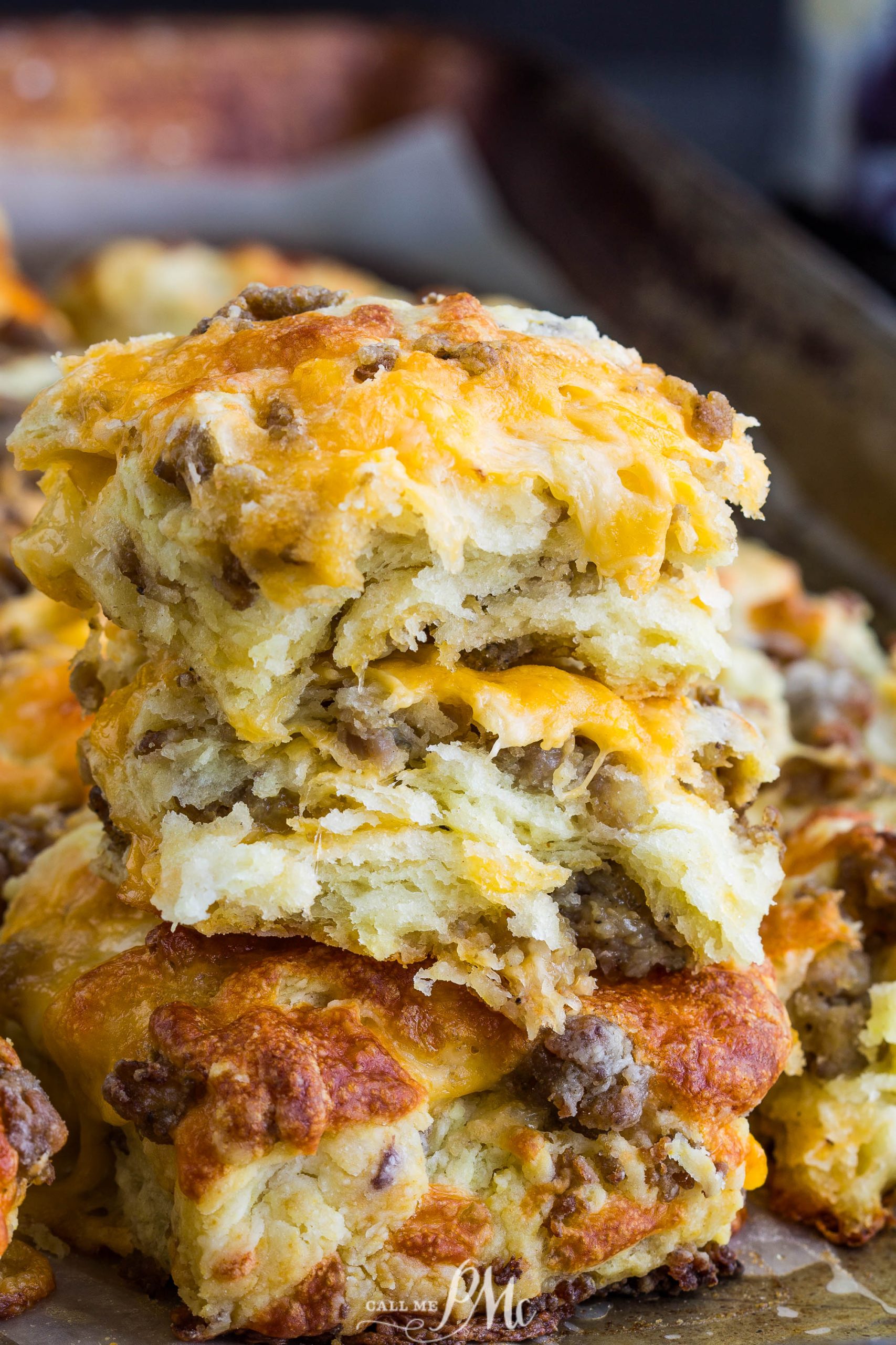 A close-up of three stacked, flaky Homemade Sausage Cheddar Biscuits on a baking tray, with golden-brown tops and visible sausage pieces.