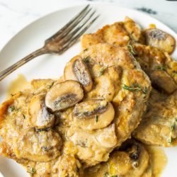 A plate of smothered pork chops topped with a creamy mushroom sauce, served with a fork on the side.