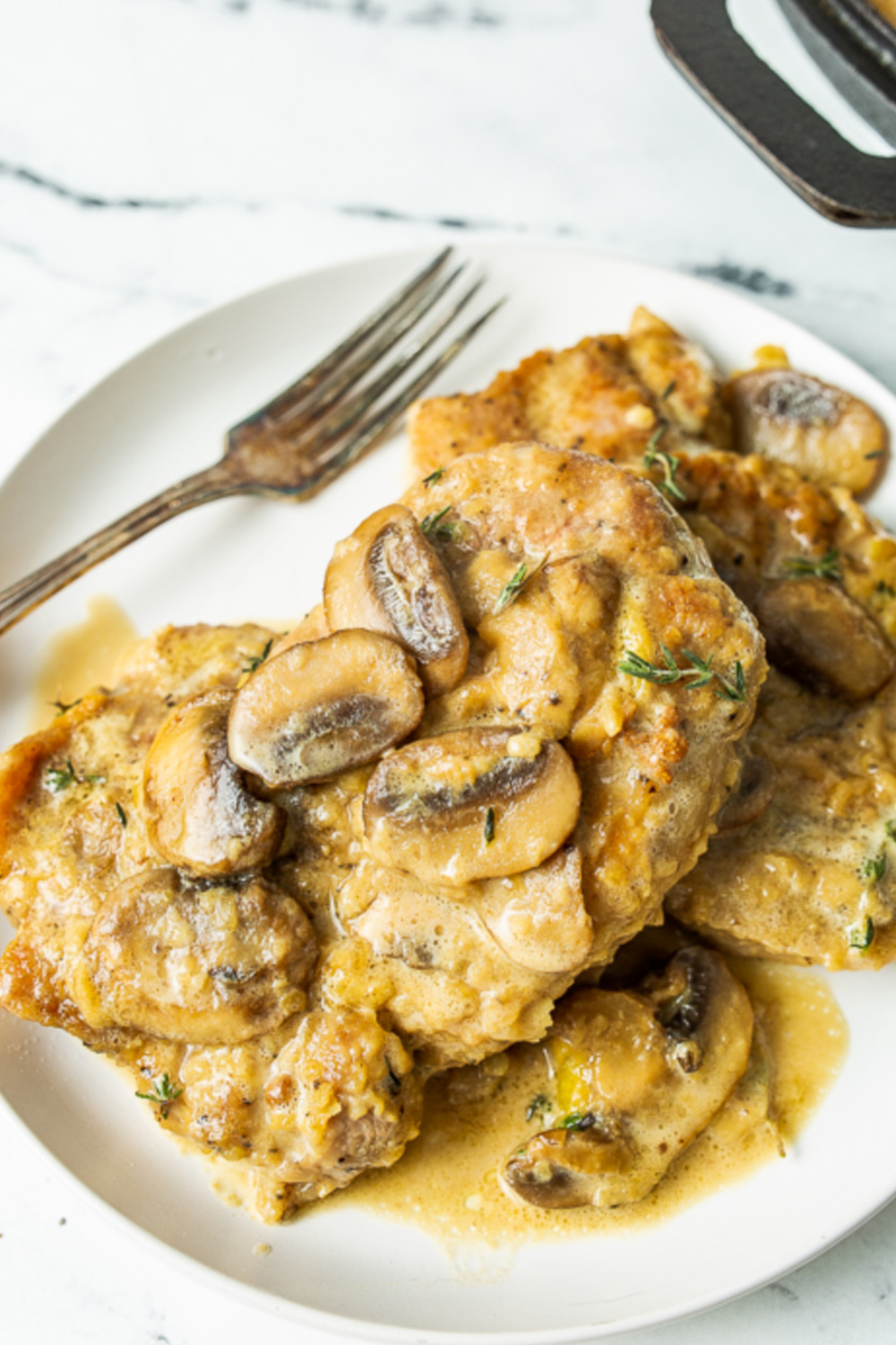 A plate of smothered pork chops topped with a creamy mushroom sauce, served with a fork on the side.