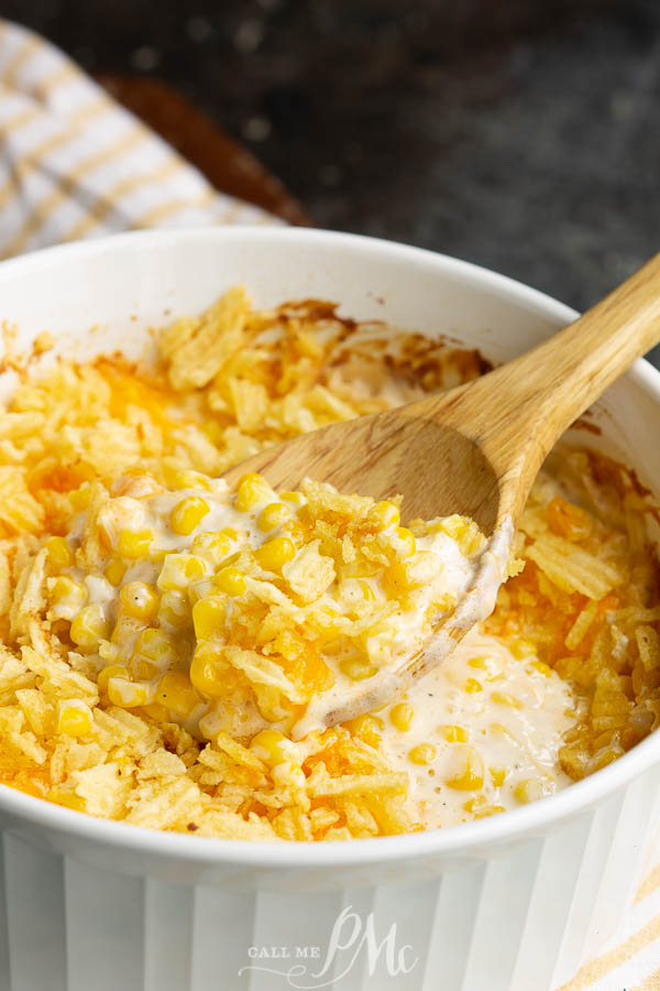 Creamy corn casserole in a white dish with a wooden spoon.