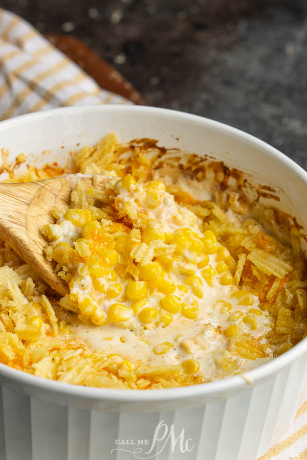 Cheesy creamy corn casserole in a white dish with a wooden spoon.