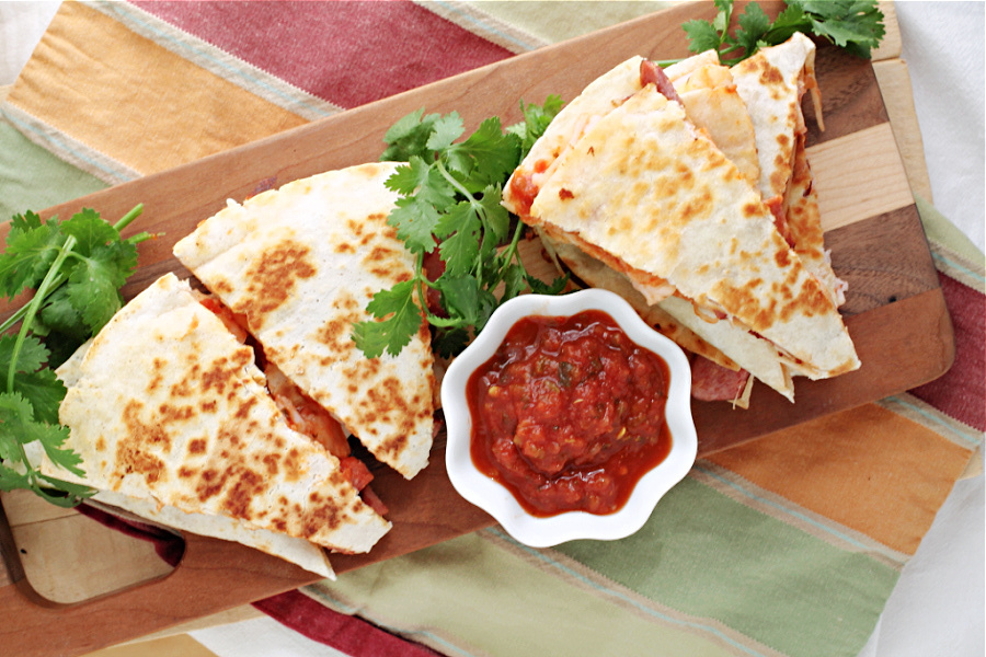 Quesadilla slices featuring savory chorizo on a wooden board with a side of red salsa and fresh cilantro.