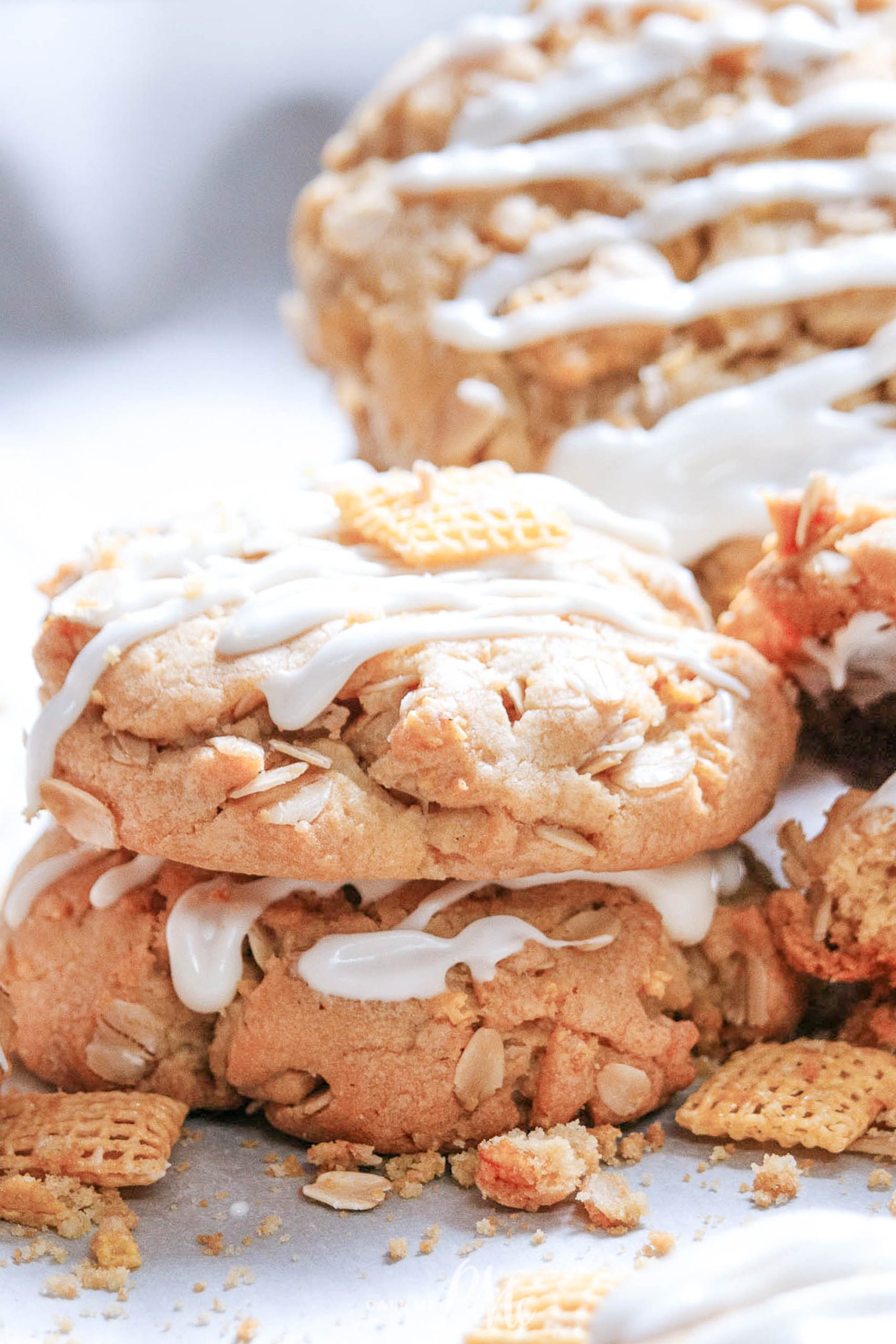 Almond Crunch Cookies with oats and cereal pieces, drizzled with white icing, stacked on a surface.