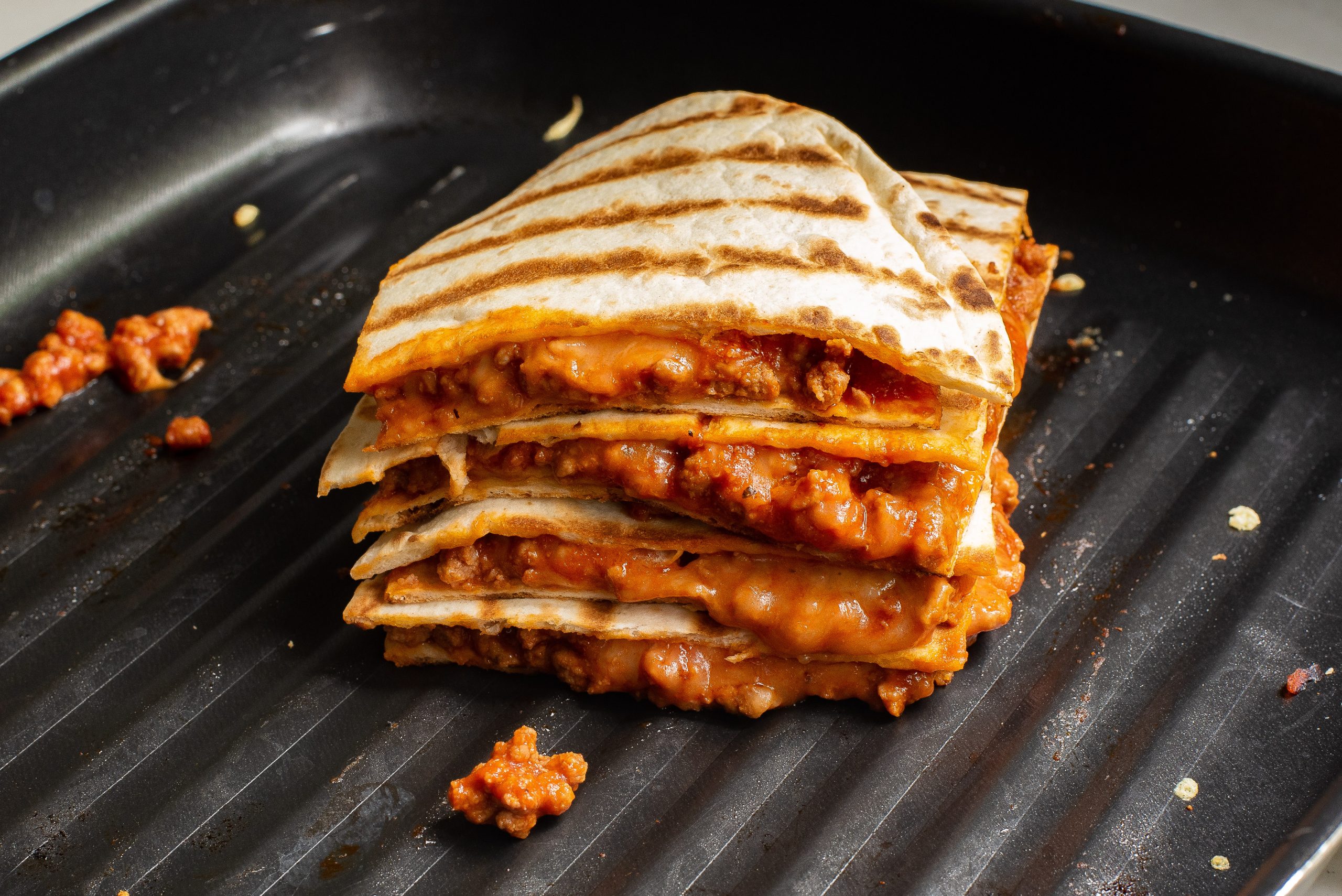 Stack of sloppy Joe quesadillas, packed with juicy meat and melted cheese, sizzling on a grill pan.