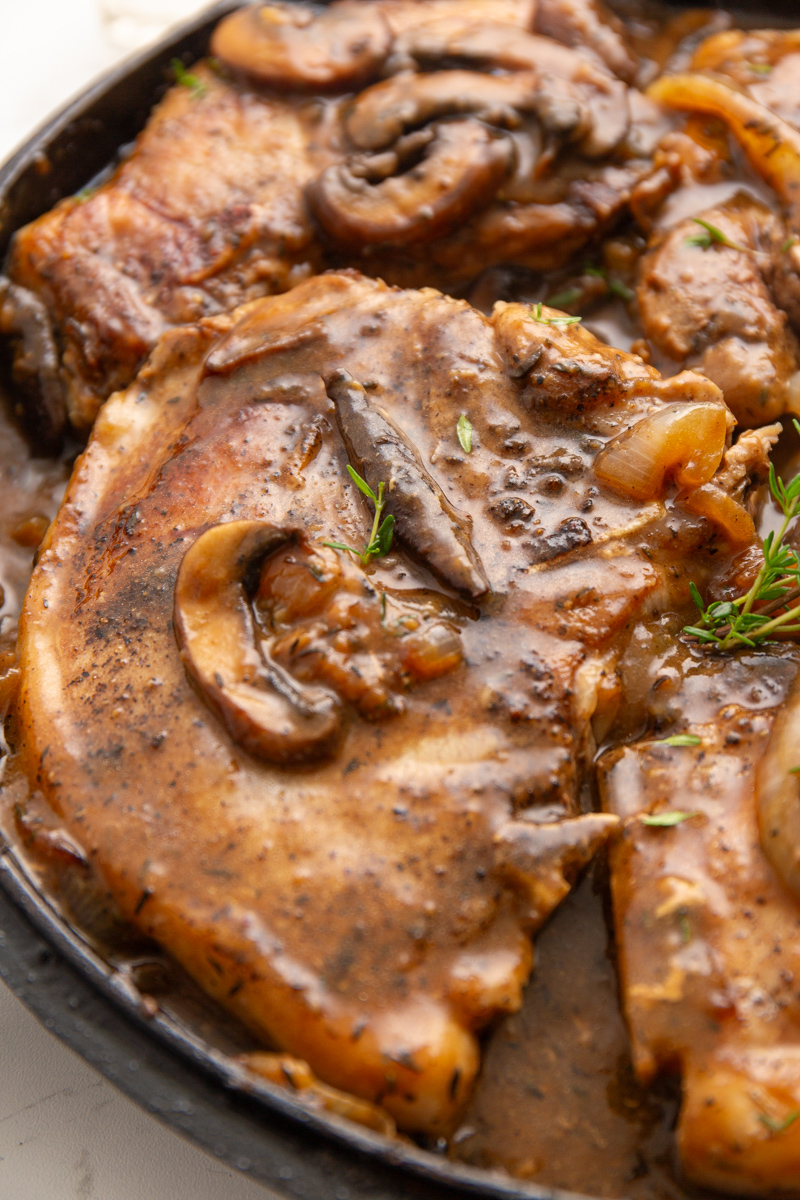 Close-up of Salisbury pork chops sizzling in a skillet, topped with mushrooms and onions in a rich sauce.