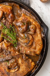 Salisbury pork chops with mushrooms and sauce in a cast-iron skillet, garnished with fresh thyme.