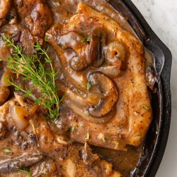 Salisbury pork chops with mushrooms and sauce in a cast-iron skillet, garnished with fresh thyme.