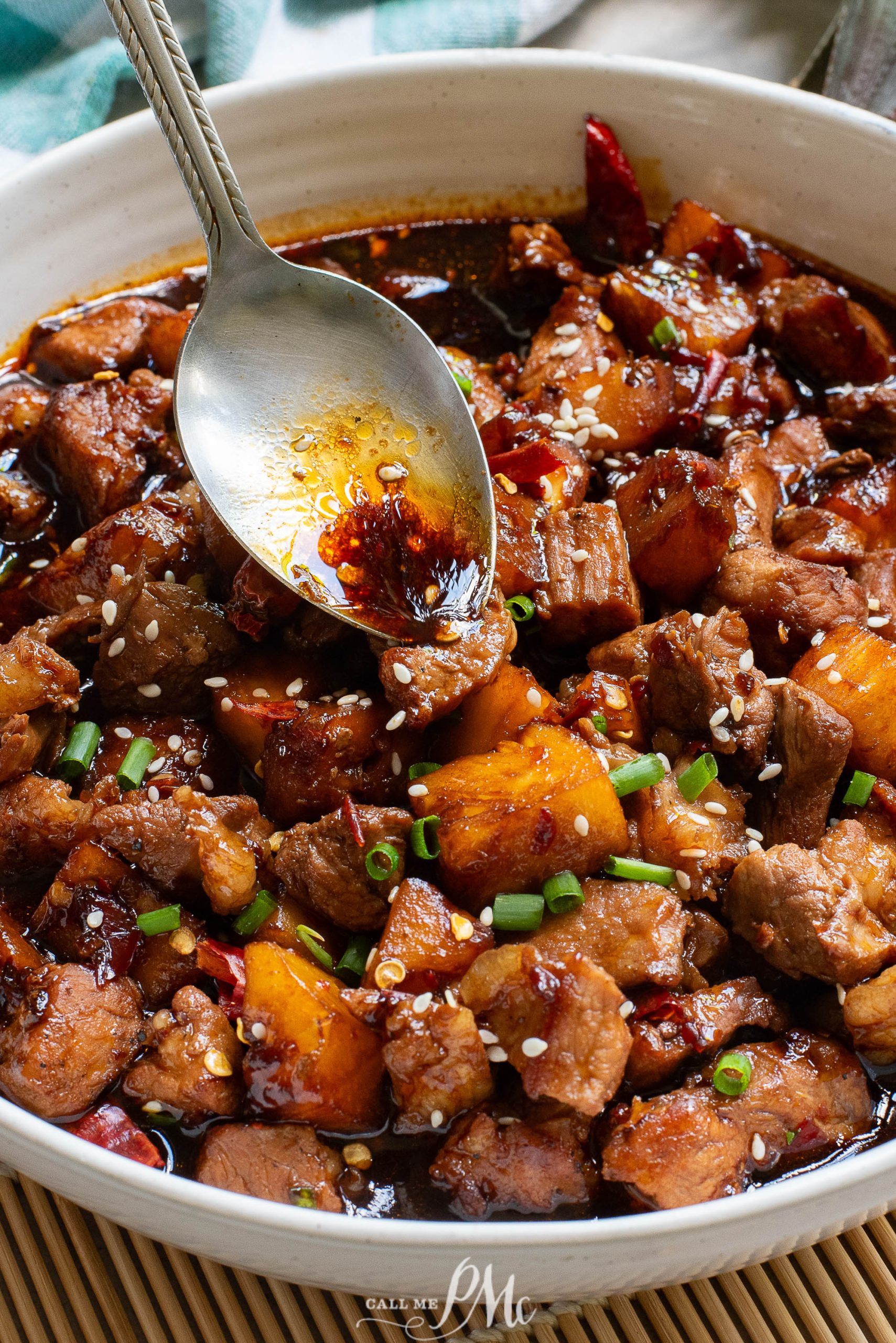 A bowl of chinese pork in a sauce with a spoon.