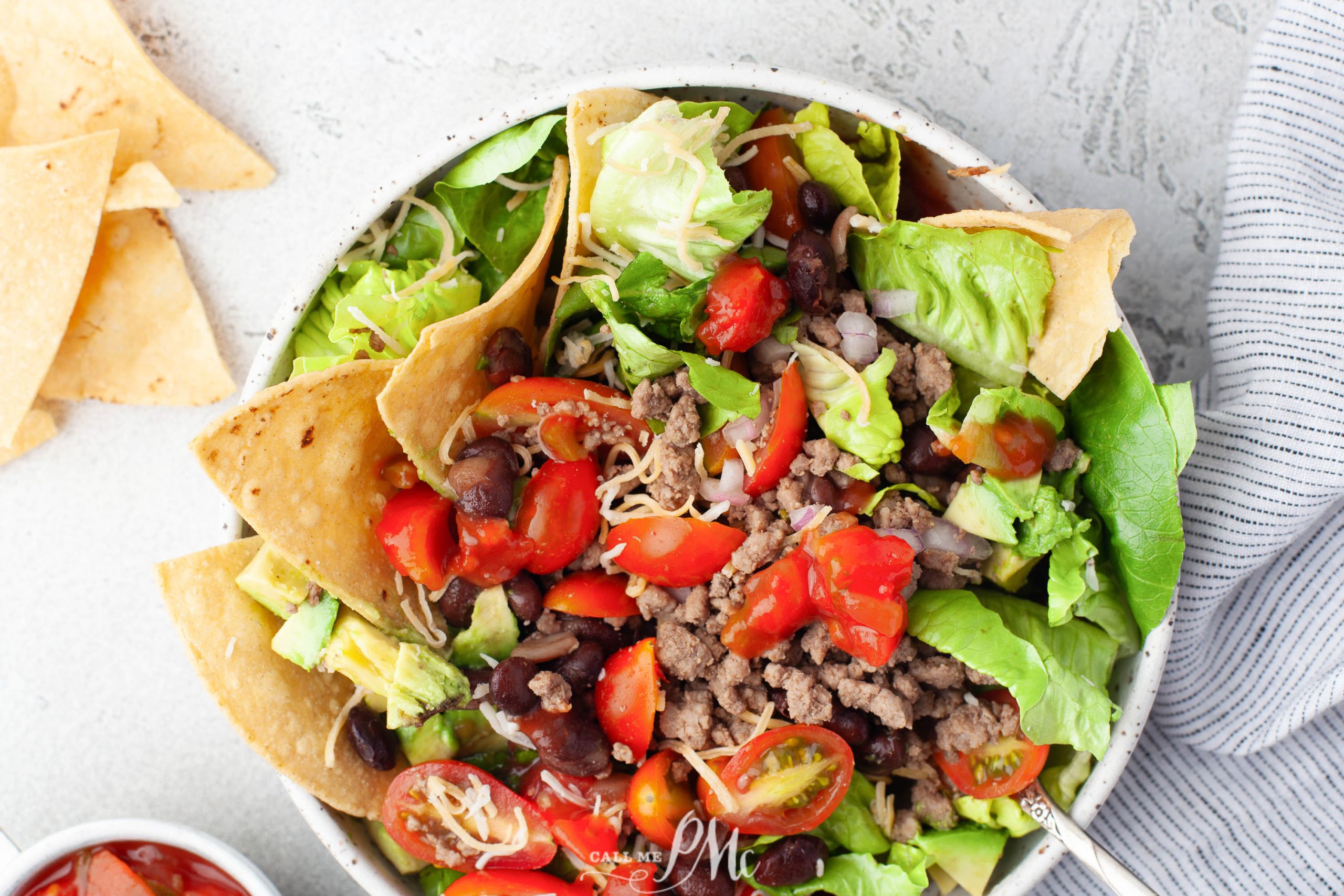 A bowl of taco salad with black beans, tomatoes, lettuce and tortilla chips.