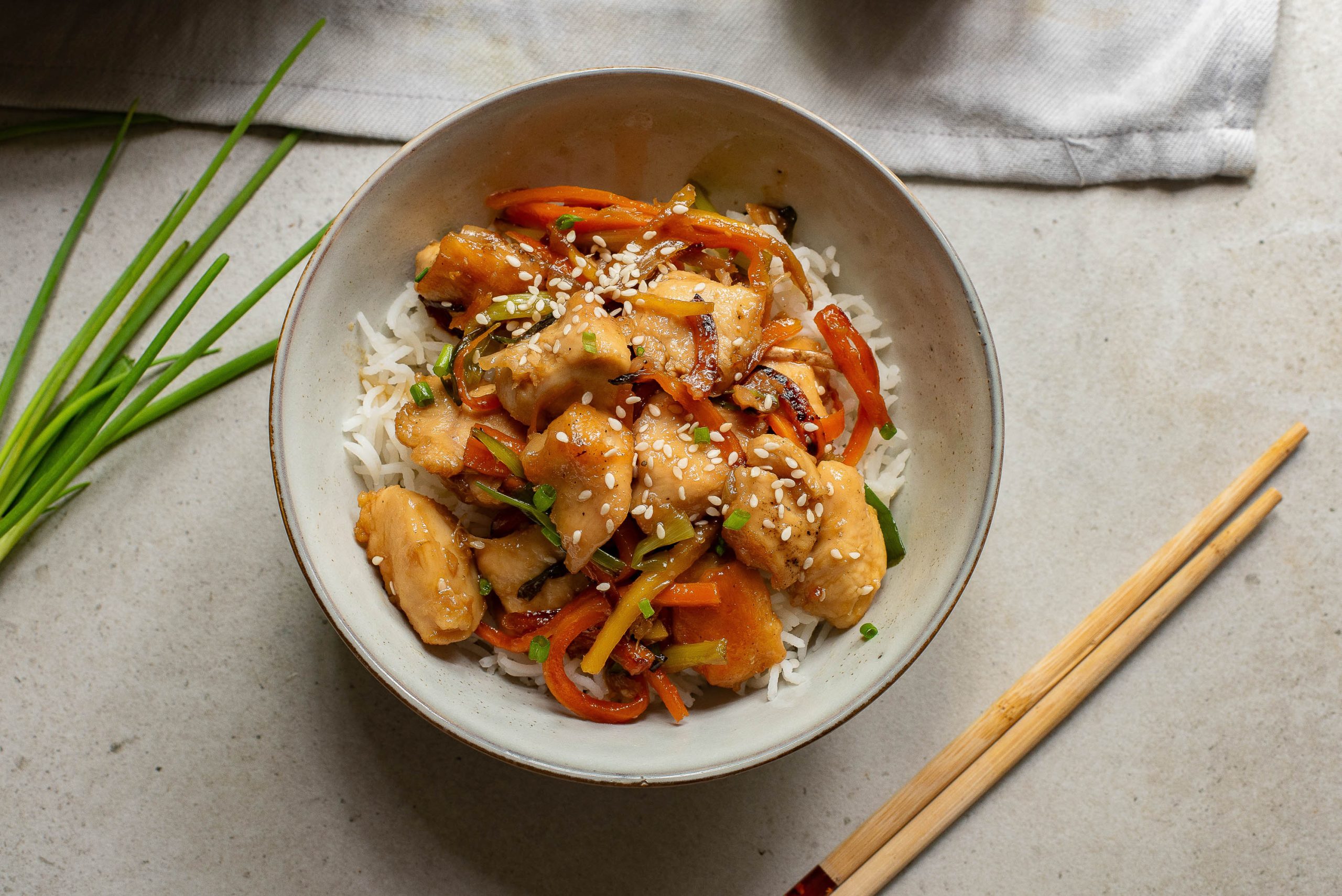 A bowl of stir fried chicken and vegetables with chopsticks.