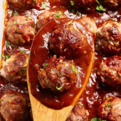 A wooden spoon with meatballs in a casserole.