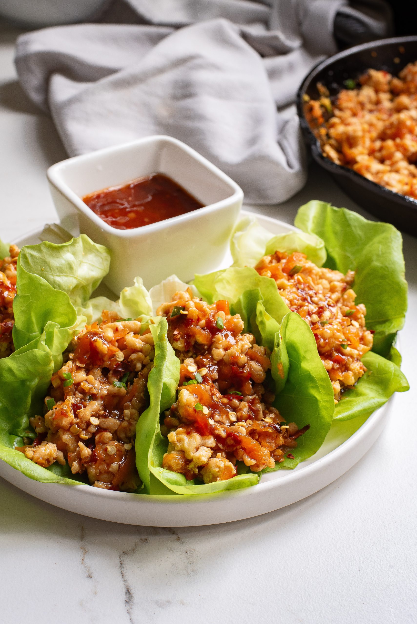Lettuce filled with stir-fried ground meat and vegetables, served with a side of dipping sauce on a white plate.