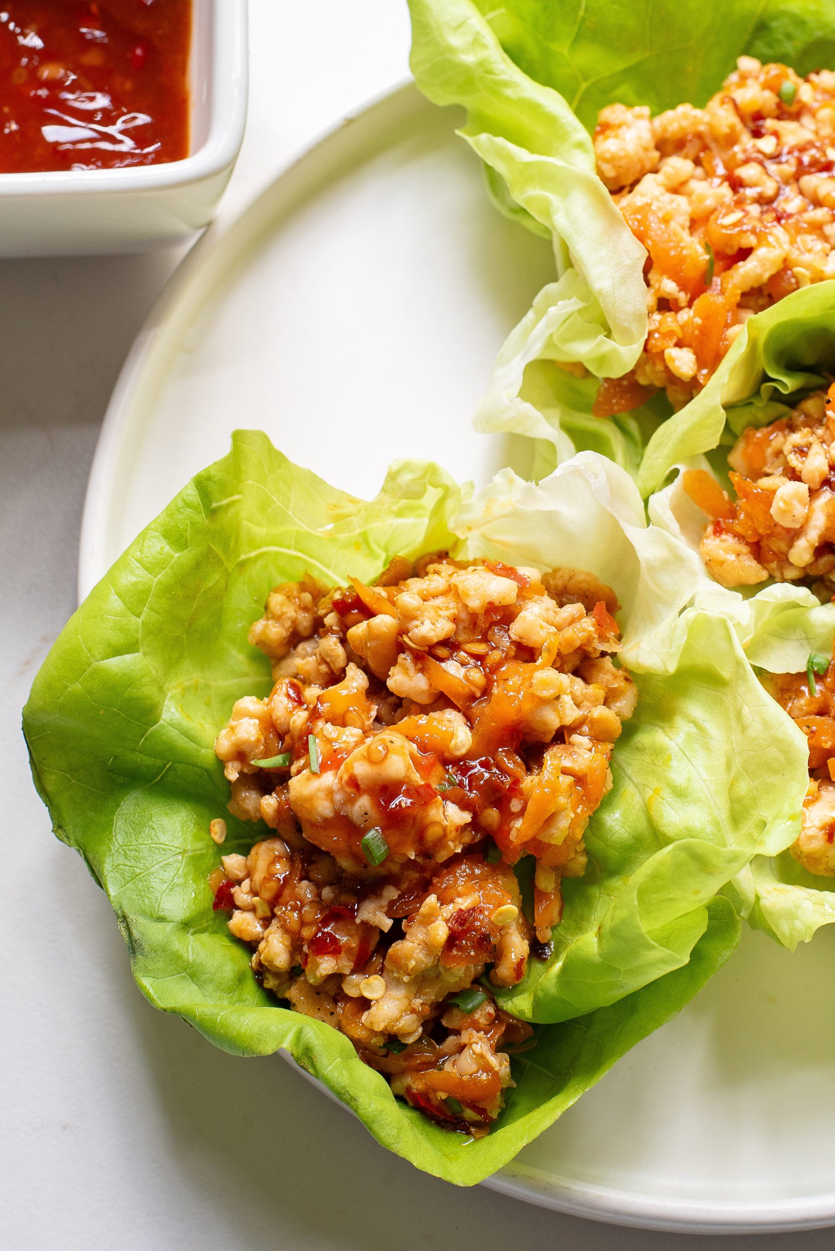 A plate of chicken lettuce wraps beside a bowl of dipping sauce.