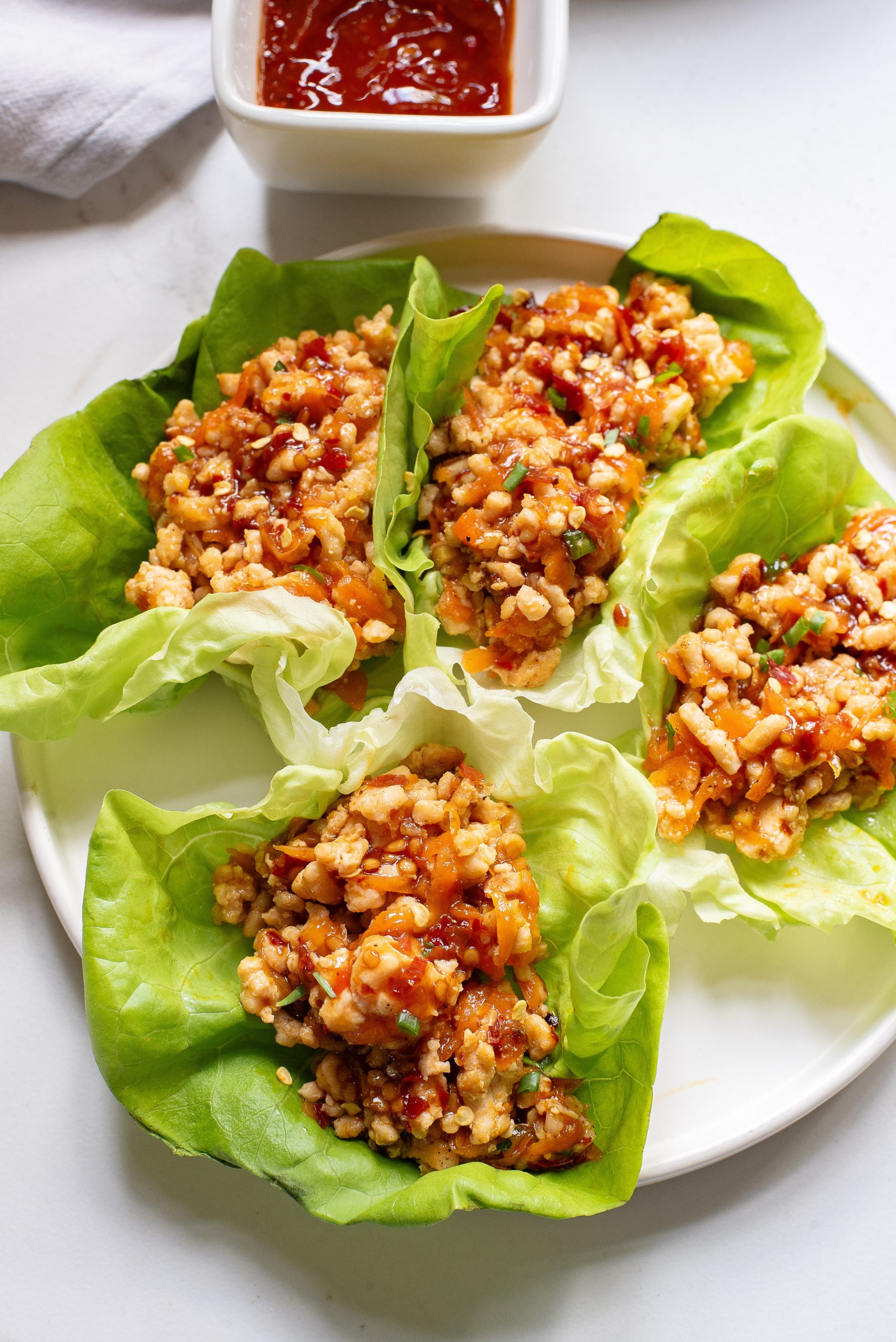 Lettuce  filled with savory minced meat and grains, served with a side of red sauce on a white plate.