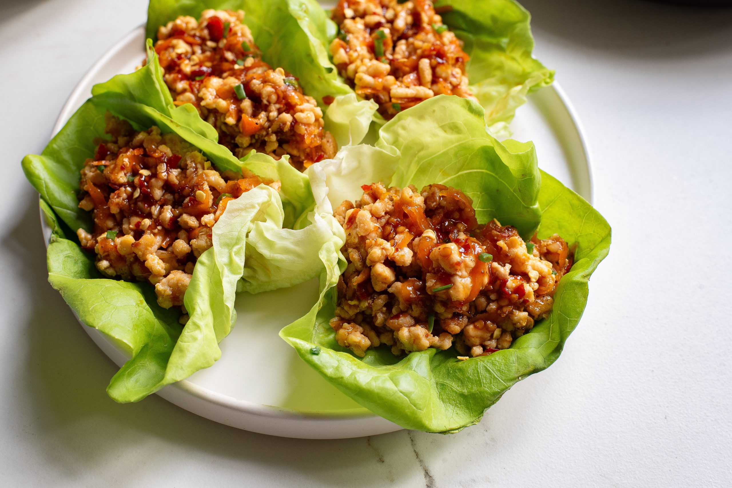 A plate of asian-style chicken lettuce wraps with a filling of ground meat, vegetables, and sauce.
