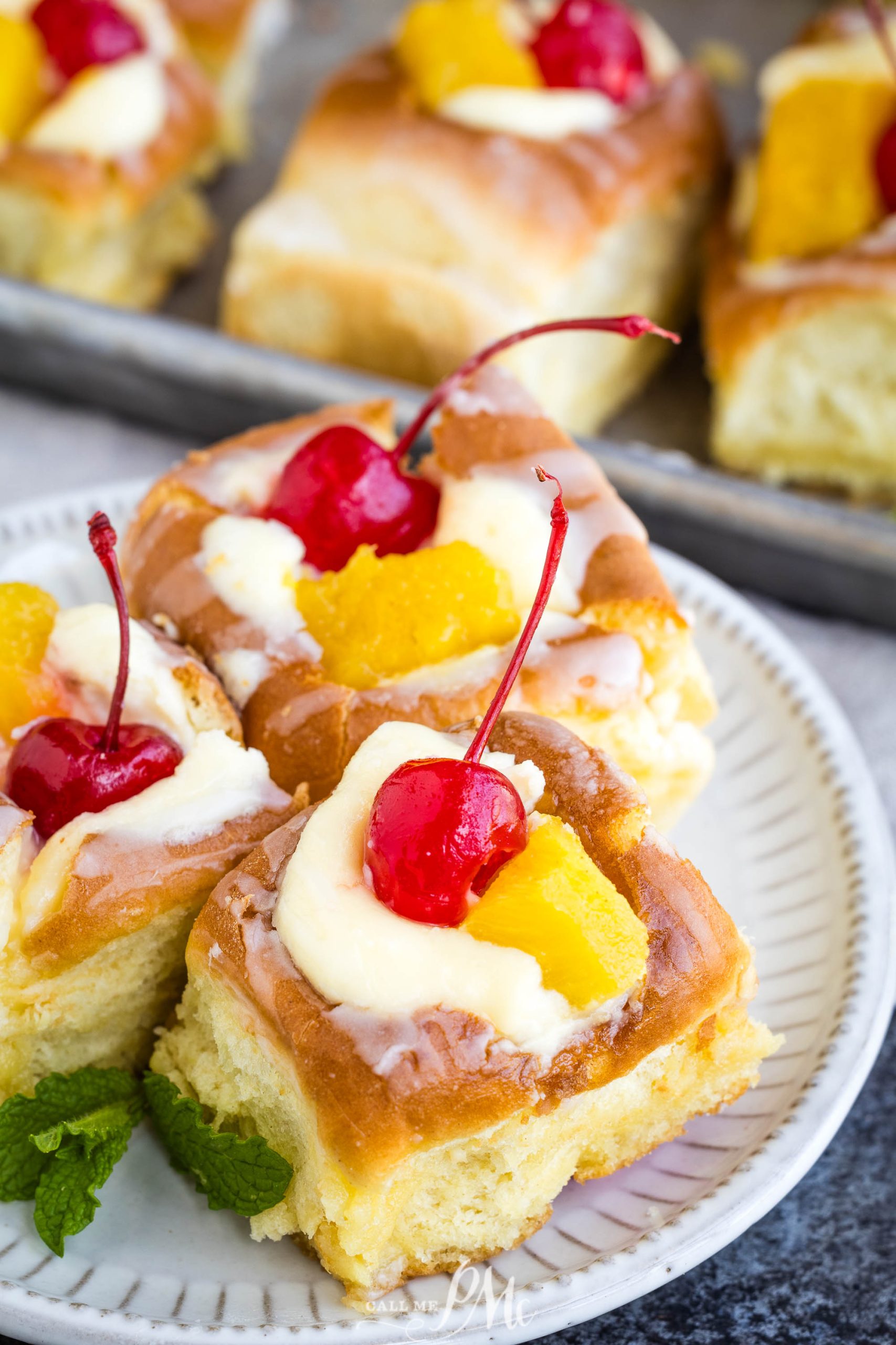 A plate of fruit-topped sweet rolls with glaze, garnished with cherries and mint leaves.