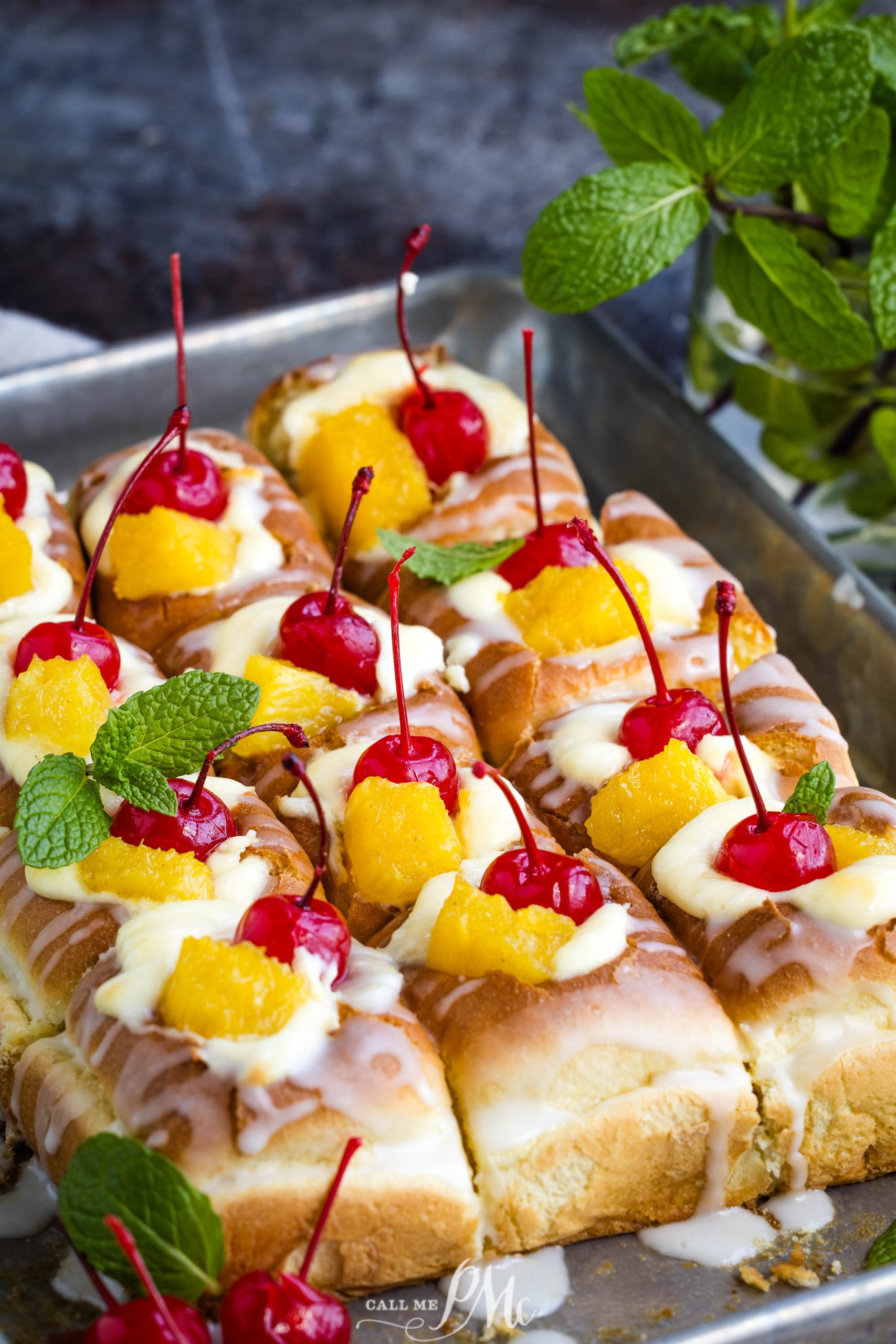 A tray of fruit-topped pastries garnished with mint leaves and cherries.