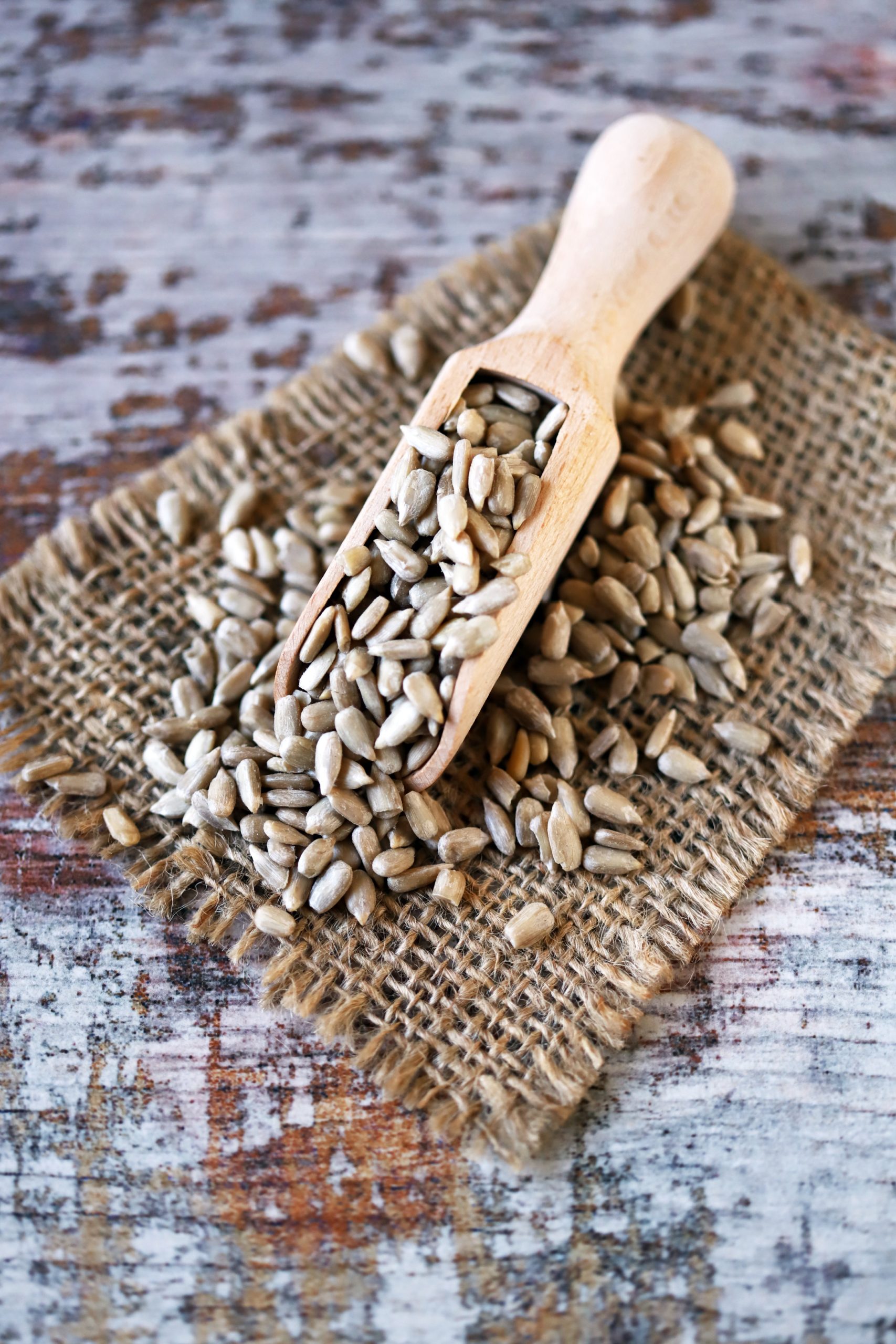 A wooden scoop filled with raw sunflower seeds, a substitute for wheat germ in recipes, on a burlap cloth with a rustic wood background.