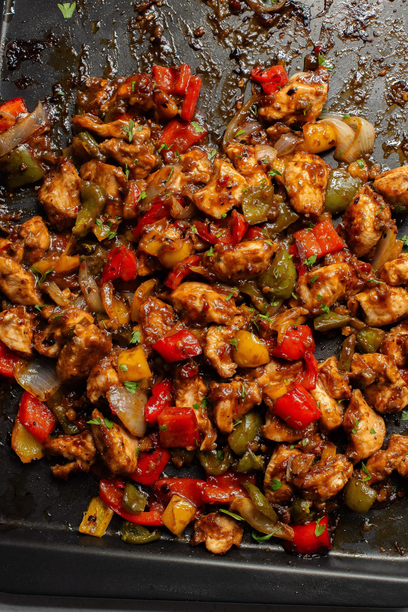 Roasted chicken with bell peppers and onions in a rich sauce on a baking sheet.