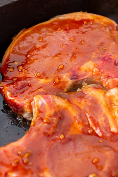 Close-up view of a piece of meat with a reddish marinade cooking in a black pan.