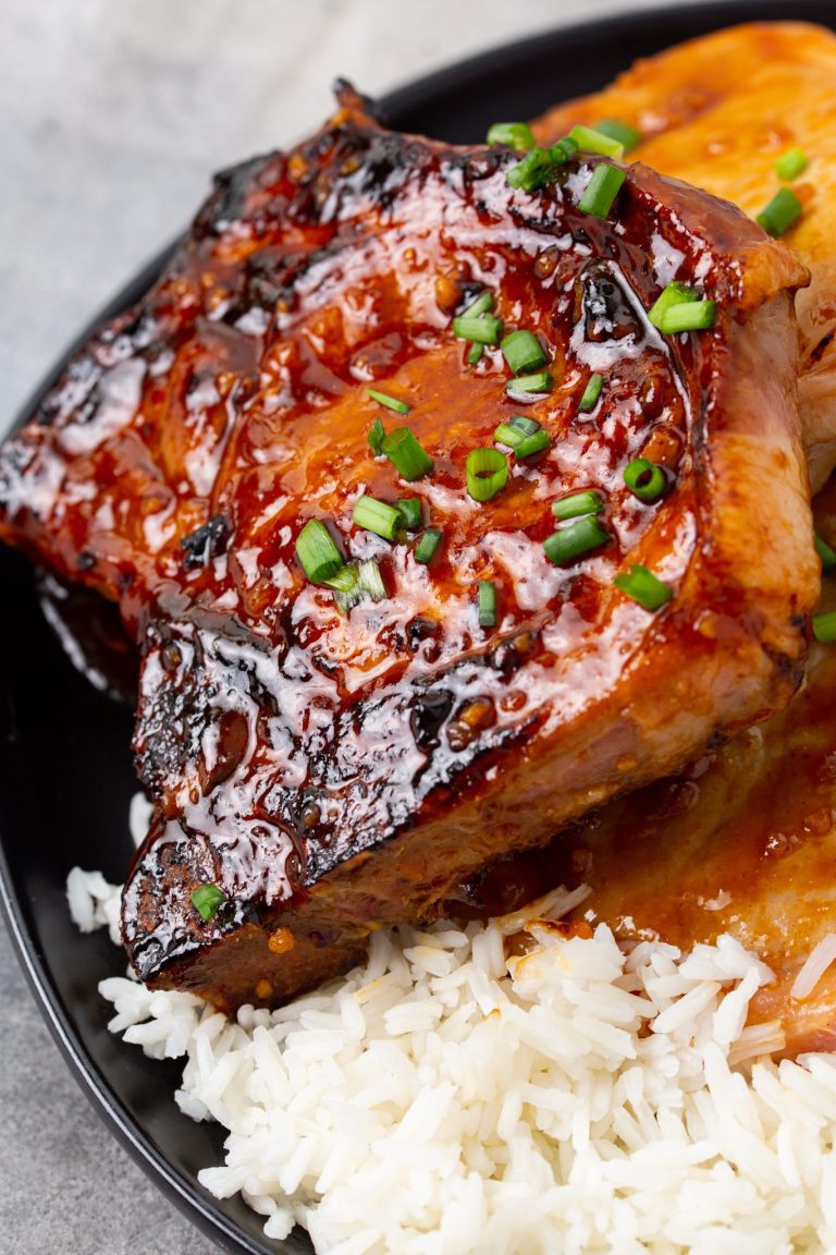 A plate of glazed grilled pork chops garnished with chopped green onions, served over a bed of white rice.