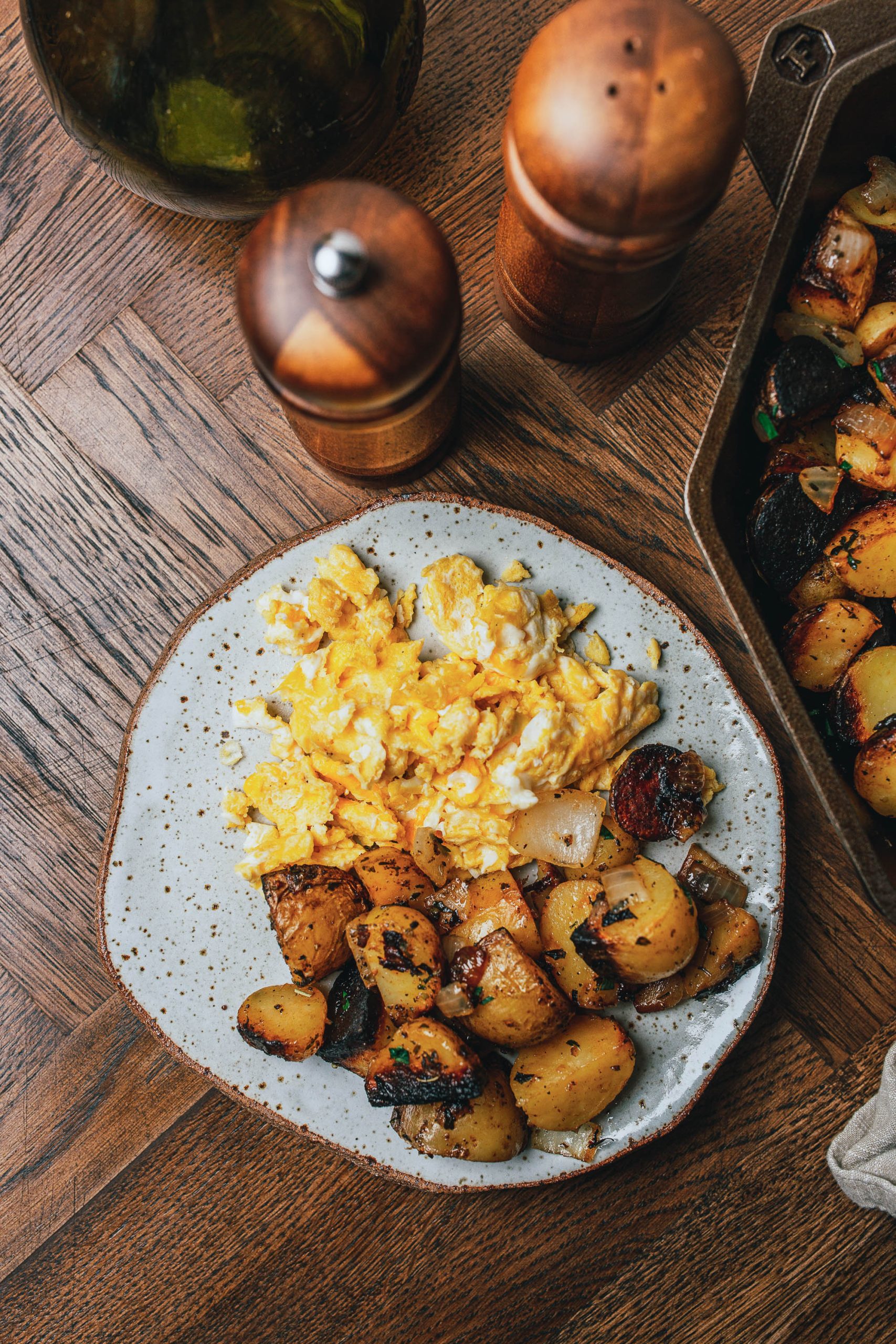 A plate of scrambled eggs and roasted potatoes on a wooden table with a pepper grinder and salt shaker nearby.