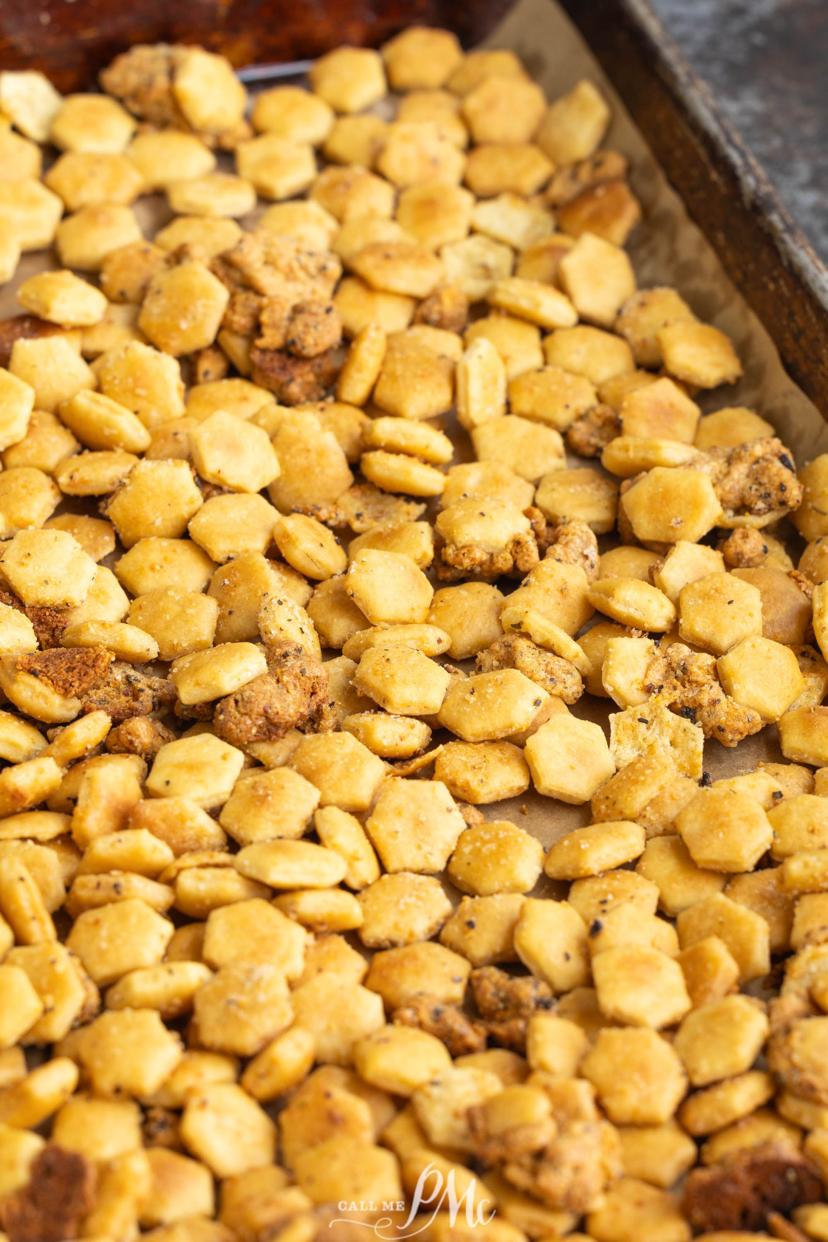 A close-up of baked oyster crackers covered in seasoning on a baking sheet.