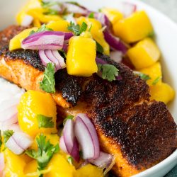 Grilled salmon topped with a mango and red onion salsa, garnished with cilantro, served in a white bowl.