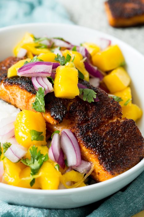 Grilled salmon topped with a mango and red onion salsa, garnished with cilantro, served in a white bowl.