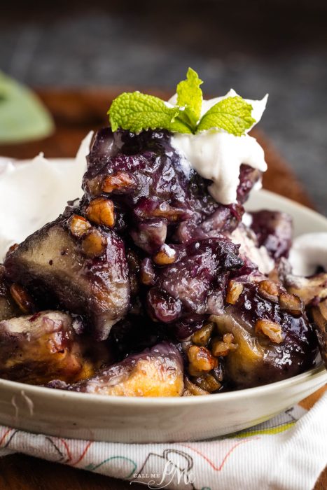 A close-up of a dessert featuring baked purple sweet potatoes topped with nuts, whipped cream, and a mint leaf garnish, served in a white bowl.