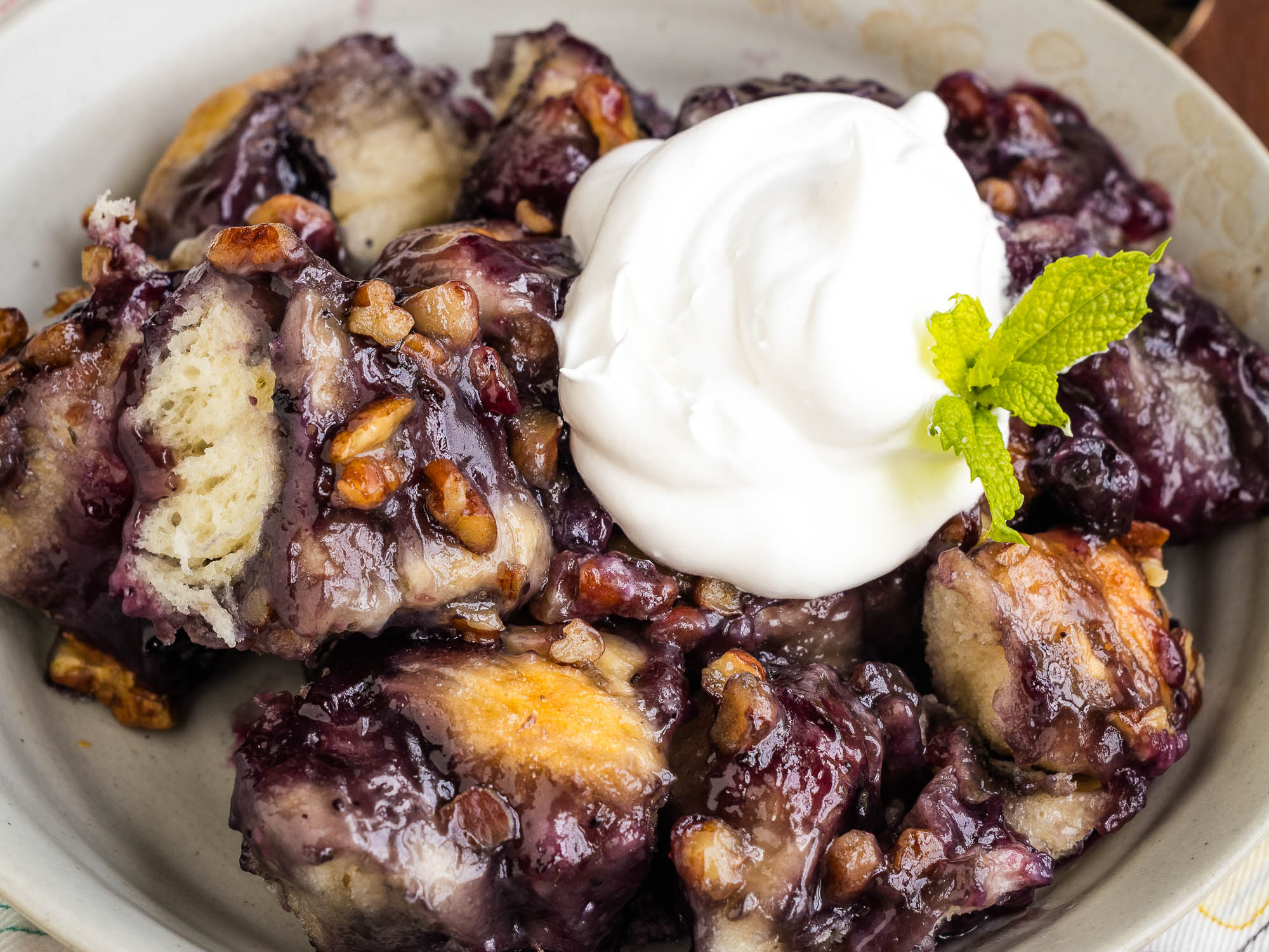 A plate of blueberry monkey bread topped with a dollop of whipped cream and garnished with a mint leaf.