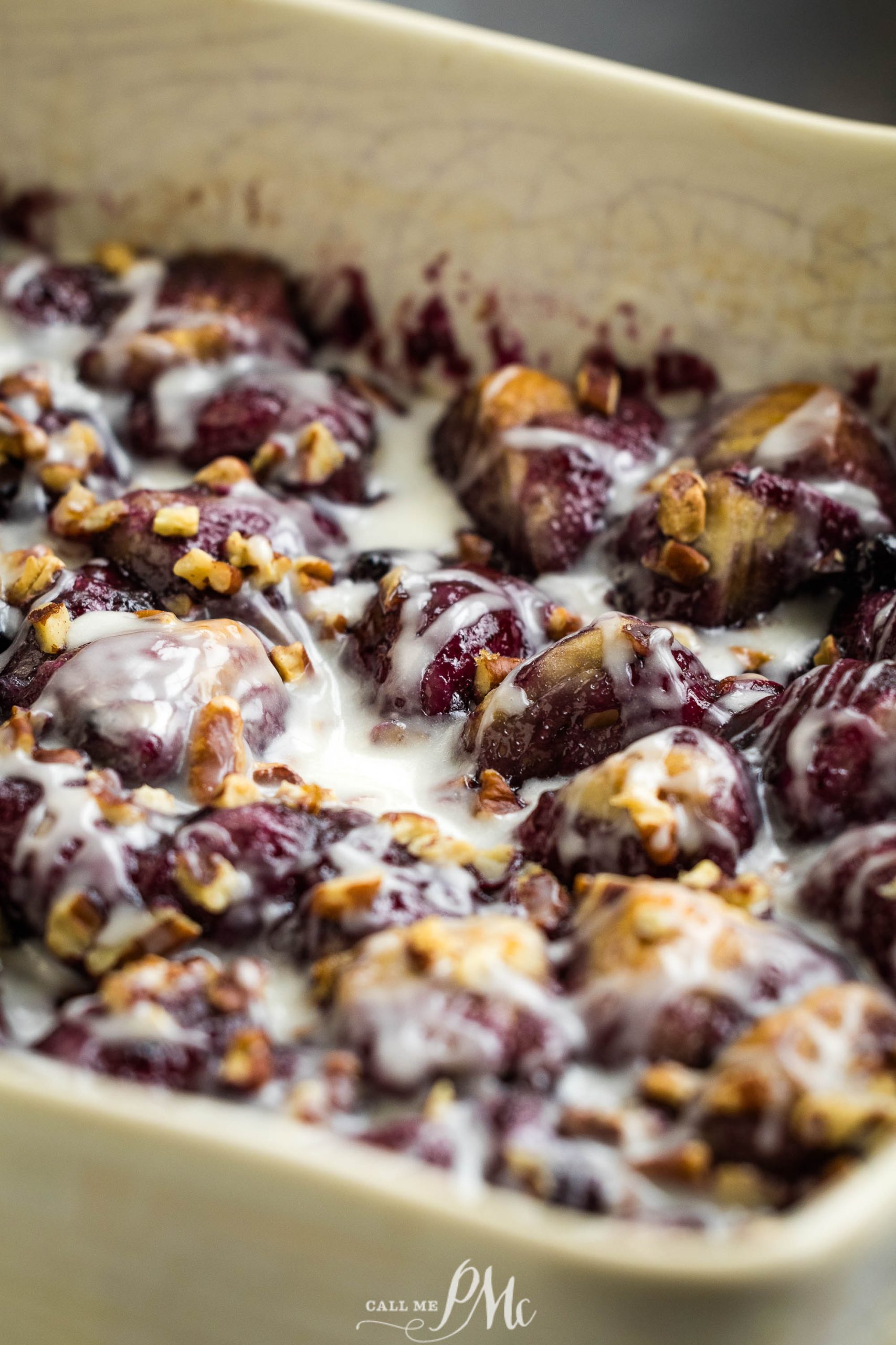 A close-up of a baked dish filled with Blueberry Cobbler Bubble-Up covered in white icing and sprinkled with chopped pecans.