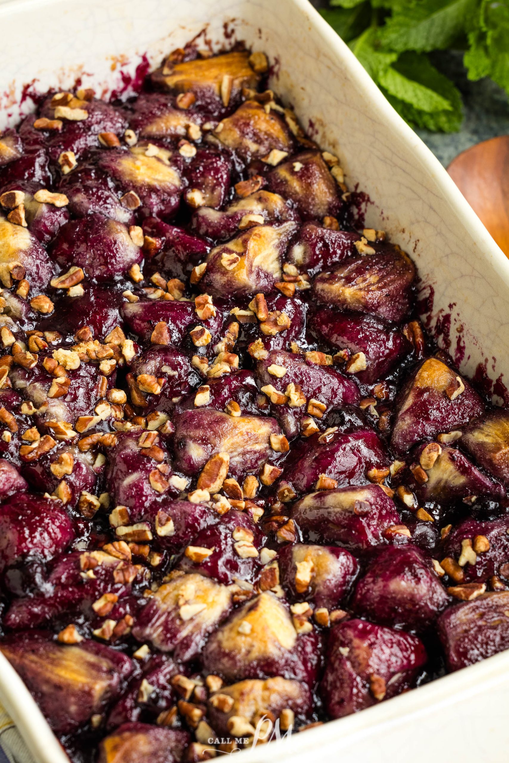 A baked Blueberry Cobbler Bubble-Up dessert featuring pieces of fruit and nuts in a rectangular dish. The fruit appears browned on the edges and is covered with a layer of crushed nuts.