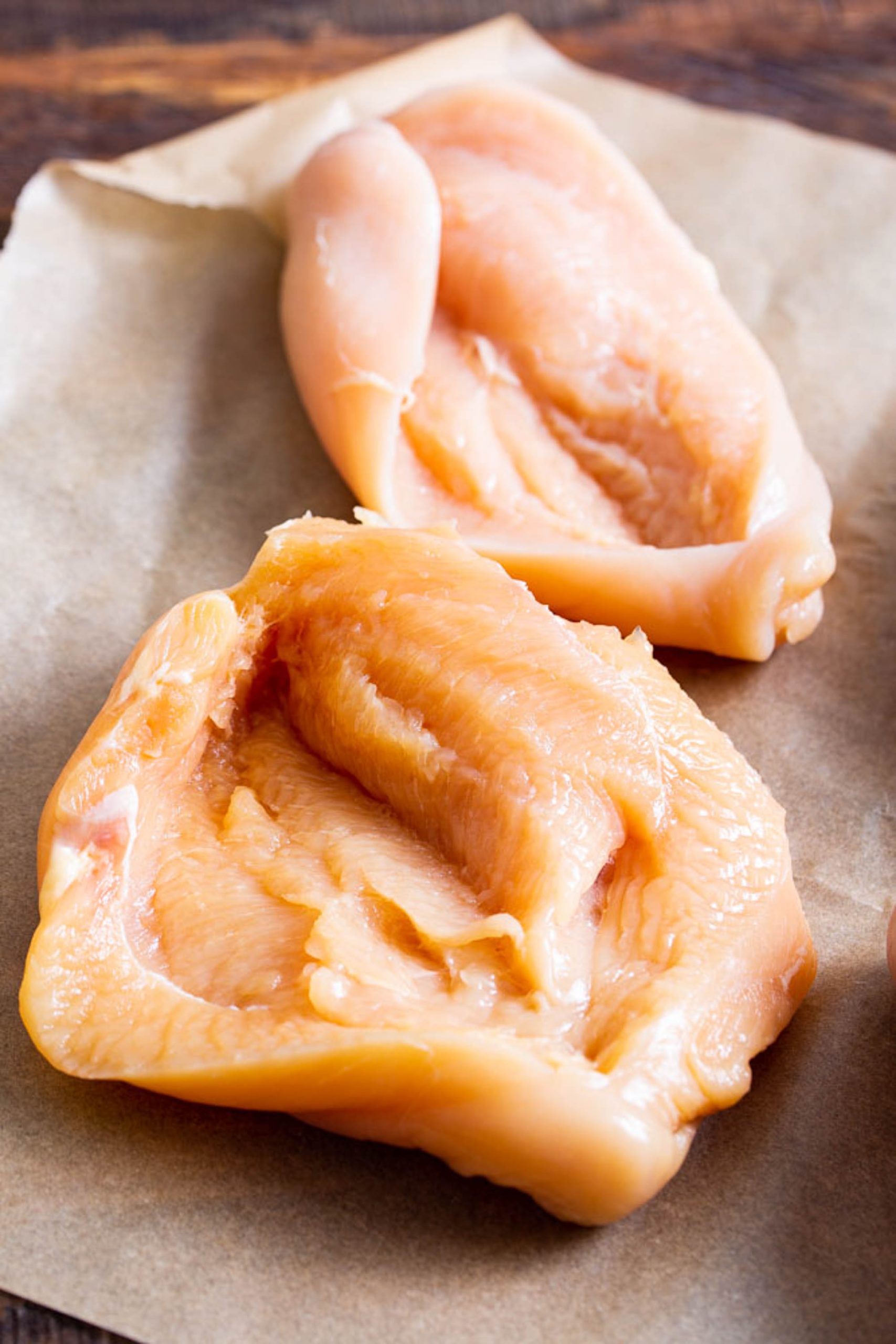 Two raw, boneless chicken breasts placed on a sheet of parchment paper.