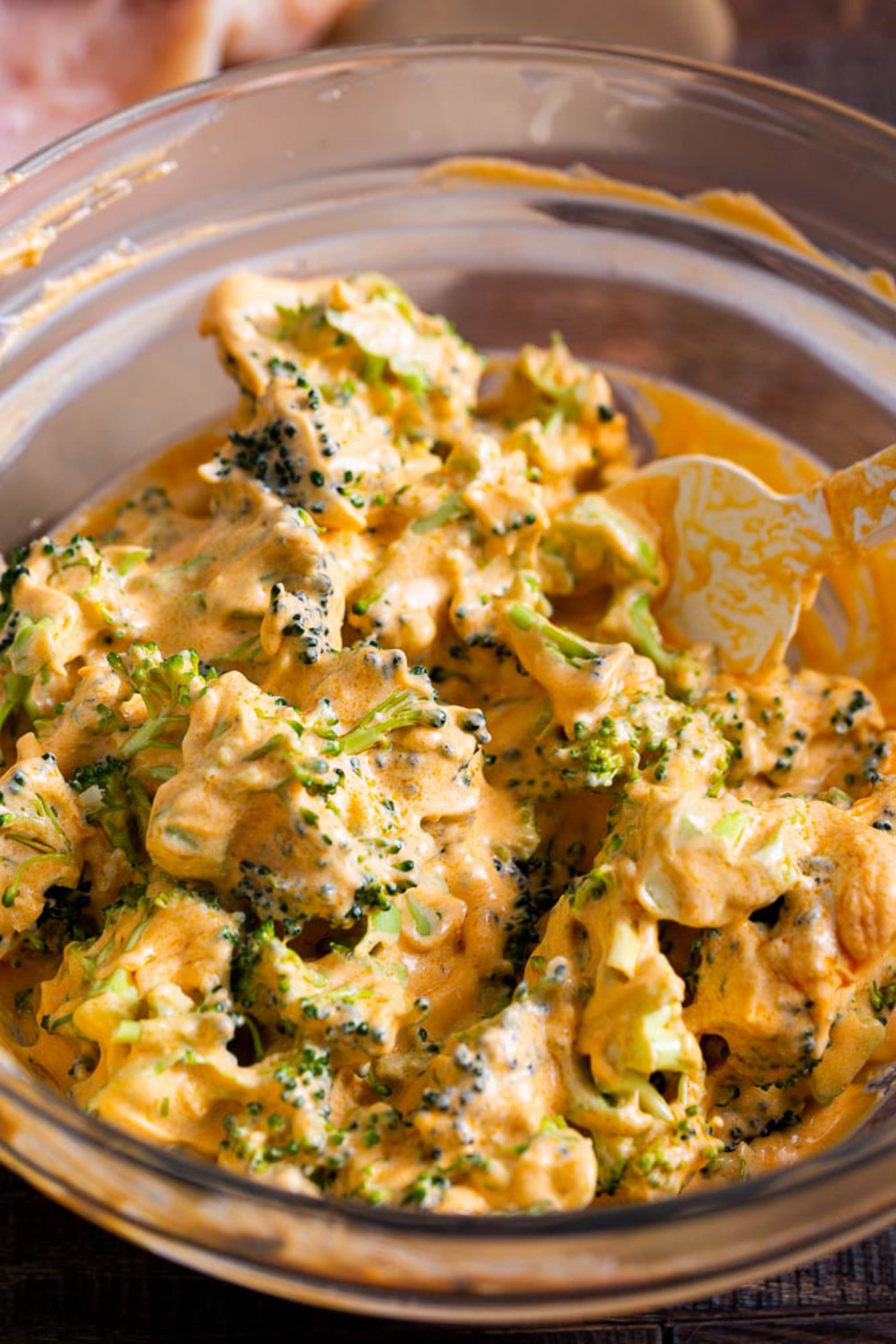 A clear glass bowl containing a creamy Broccoli Stuffed Buffalo Chicken Breasts mixture is shown. The salad is covered in a yellowish dressing.