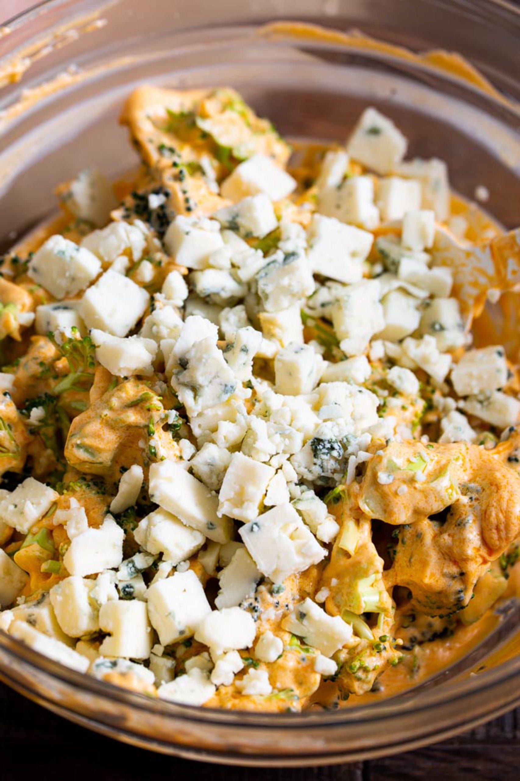 A glass bowl filled with a mixture of diced white cheese and a creamy, orange-colored ingredient, Broccoli Stuffed Buffalo Chicken Breasts.