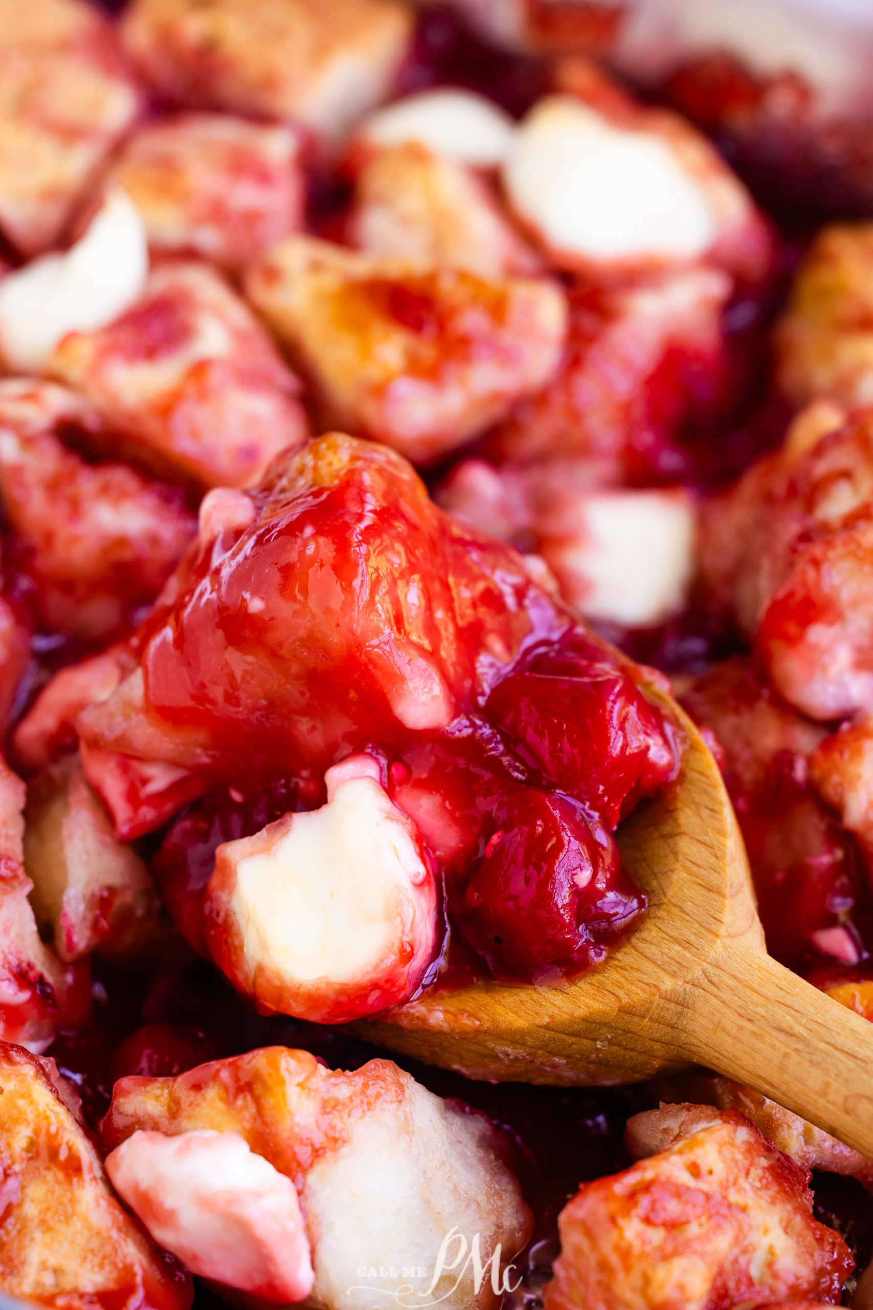 Close-up of a wooden spoon serving a mixed berry bread pudding, showing chunks of bread, creamy white cheese, and vibrant red mixed berries.