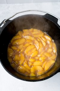 A black pot filled with cooked apple slices in a simmering brown sauce. Steam rises from the mixture, indicating it is hot.