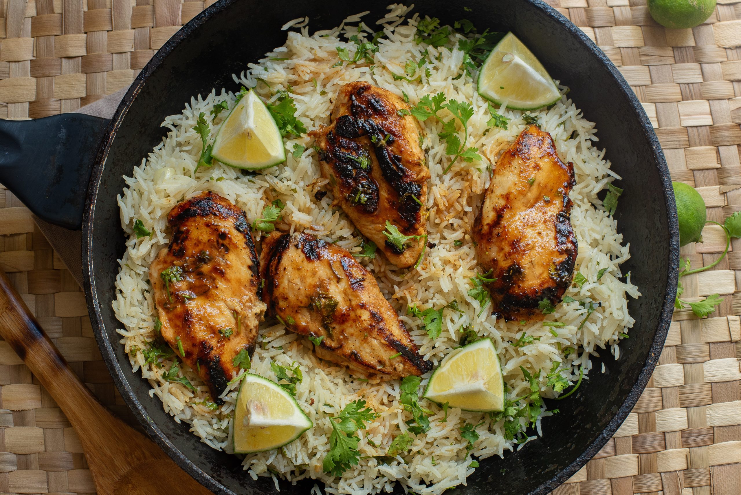 A plate of grilled chicken breast on a bed of rice, garnished with a lemon wedge and cilantro. Fork placed beside plate.