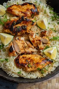 Grilled chicken breasts on a bed of seasoned rice, garnished with cilantro and lemon wedges.