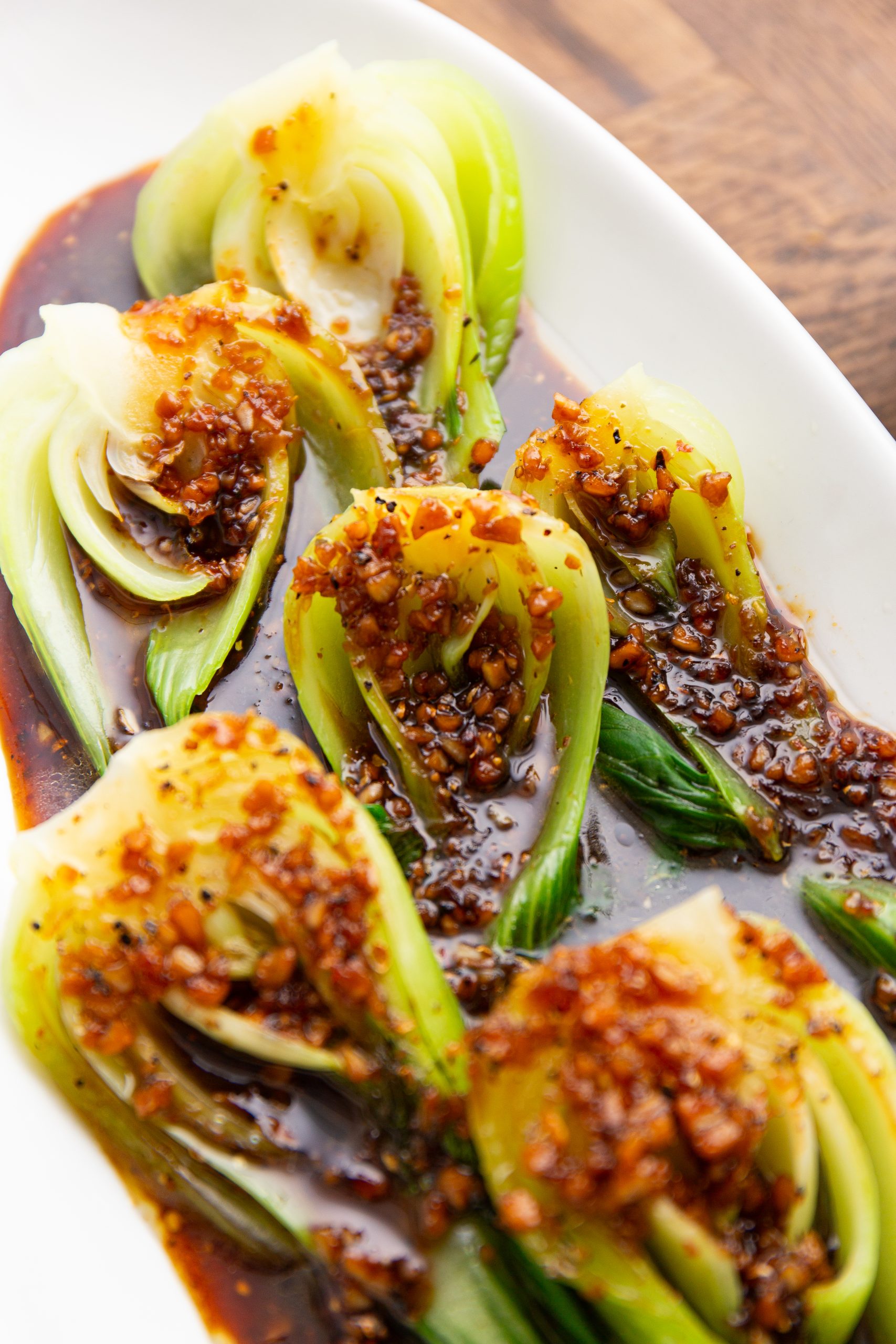 A plate of steamed bok choy topped with a savory garlic sauce, served on a wooden table.