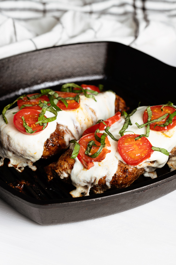 Stovetop Grilled Chicken Caprese features tender chicken breasts topped with melted mozzarella, fresh tomato slices, and basil in a black square pan.